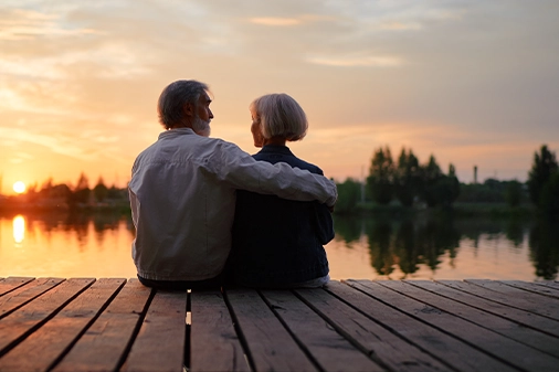 senior couple sitting on dock by the lake at sunset